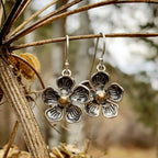 Silver flower-shaped earrings hanging from a branch with a blurred natural background