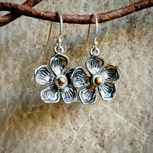 Silver flower-shaped earrings hanging from a branch on a textured surface