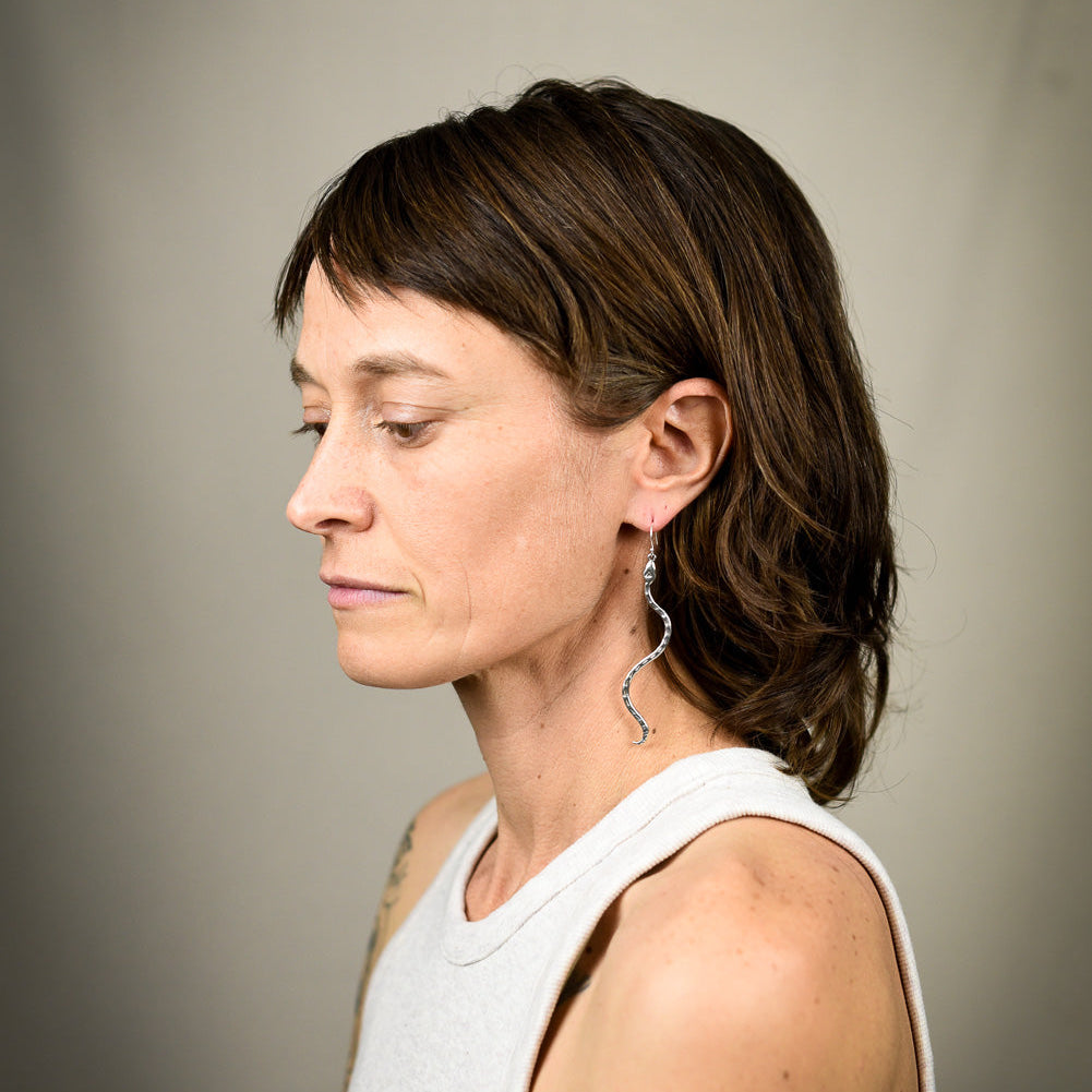Woman wearing a white sleeveless top and snake earrings 
against a plain background