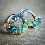 Silver hoop earrings with blue and green gemstones on a textured surface