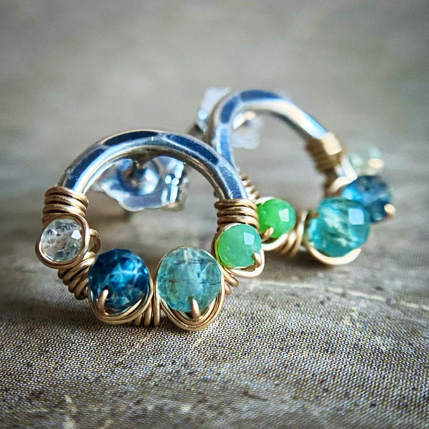 Silver hoop earrings with blue and green gemstones on a textured surface
