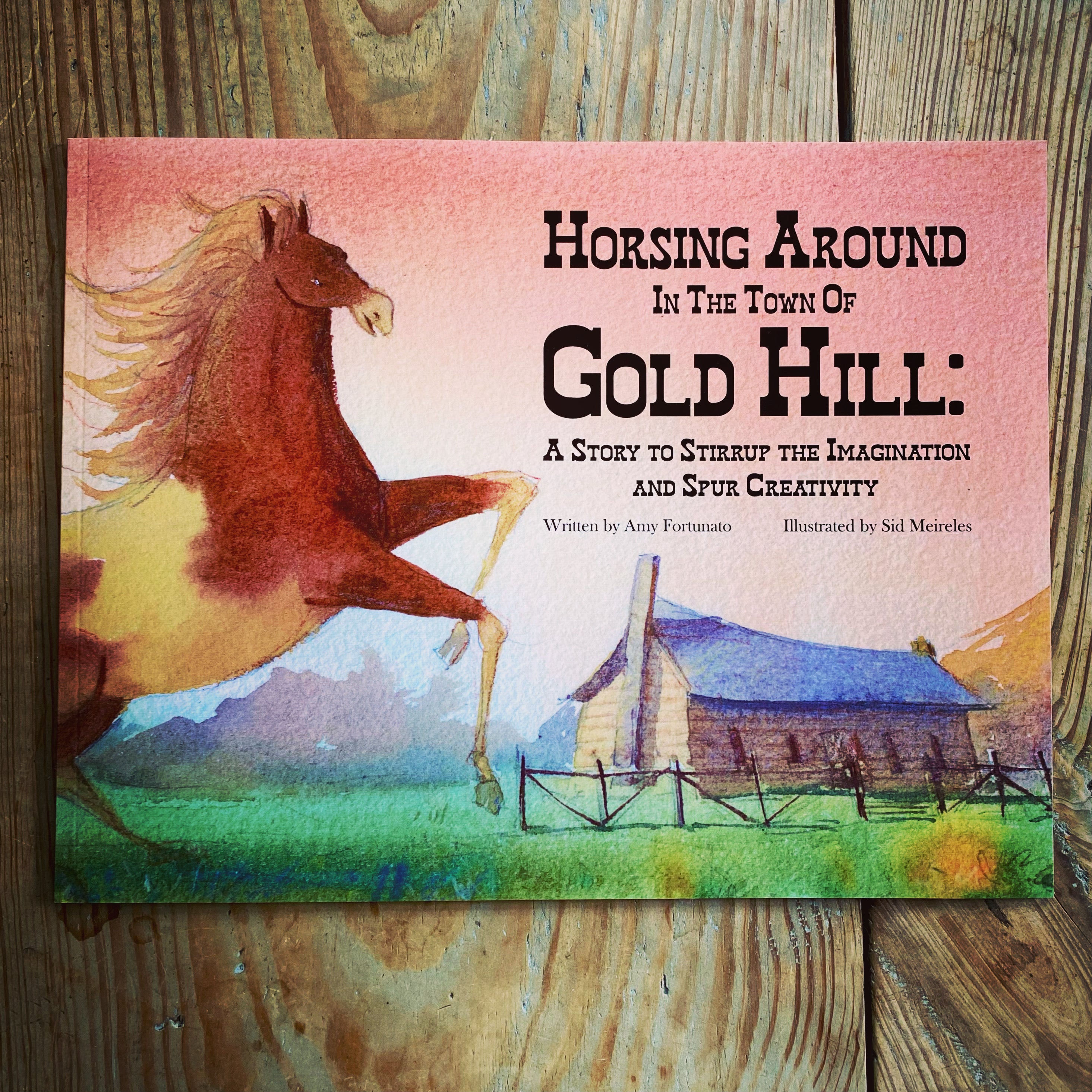 Book cover of 'Horsing Around in the Town of Gold Hill' with a horse and cabin illustration on a wooden surface.