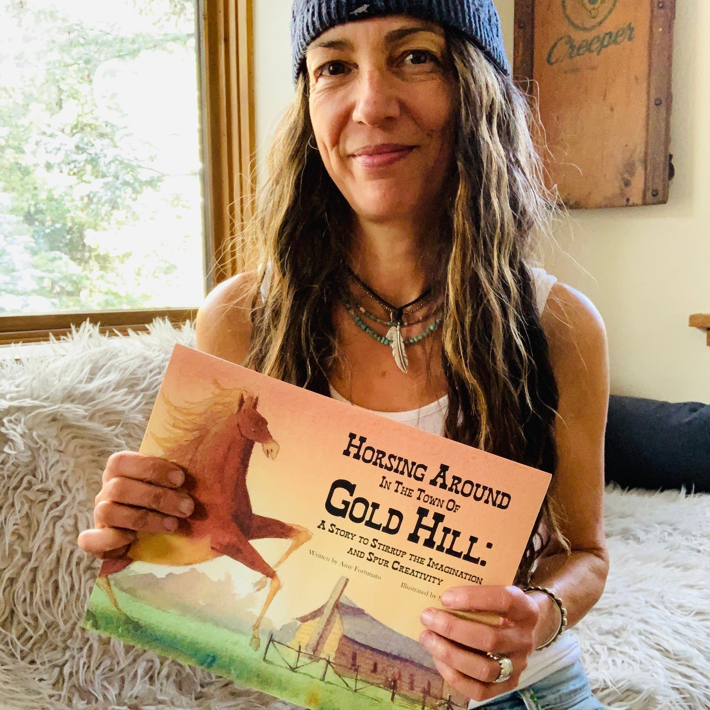 Amy holding a book titled 'Horsing Around the Town of Gold Hill' in a cozy indoor setting.