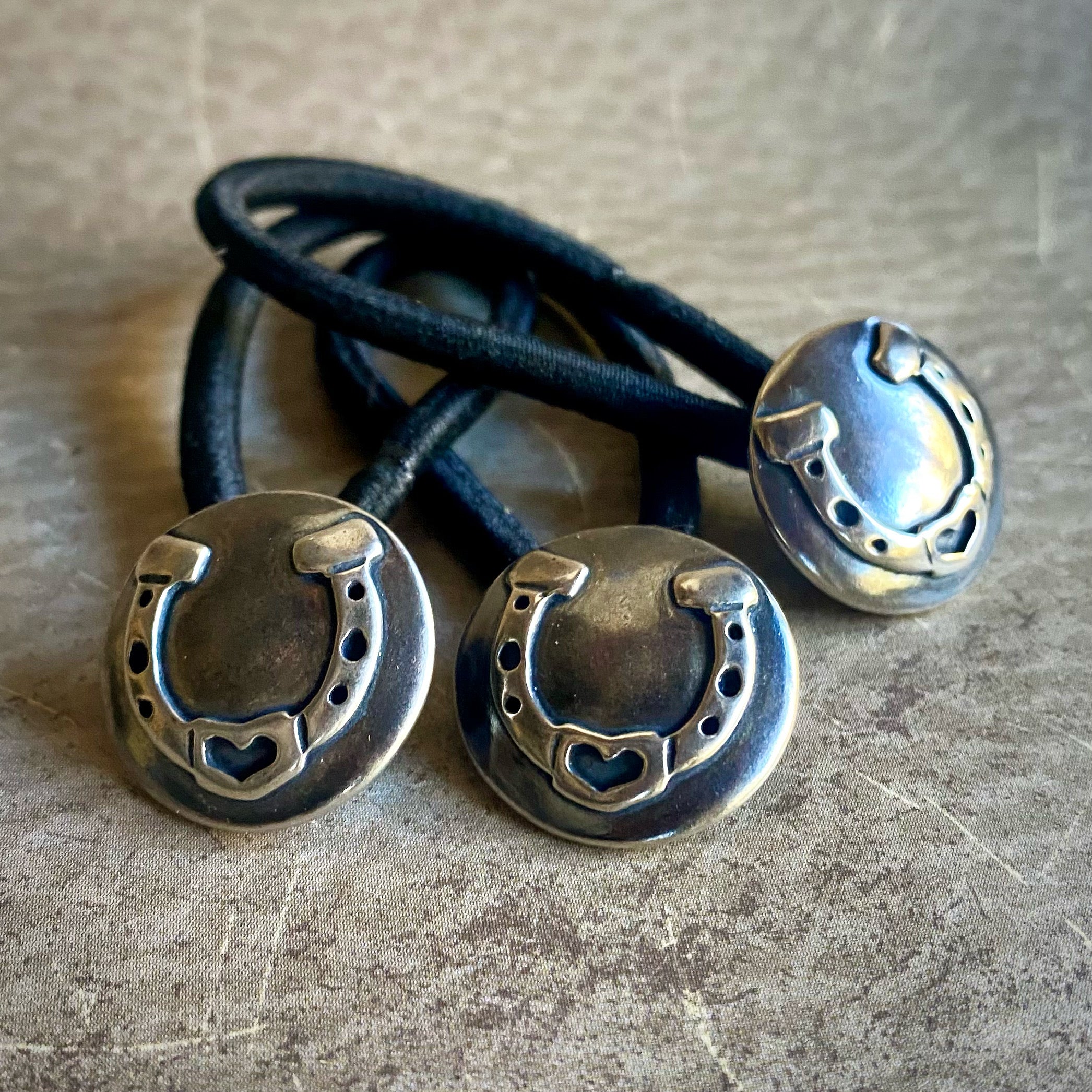Three black hair ties with silver horseshoe-shaped ends on a textured surface.