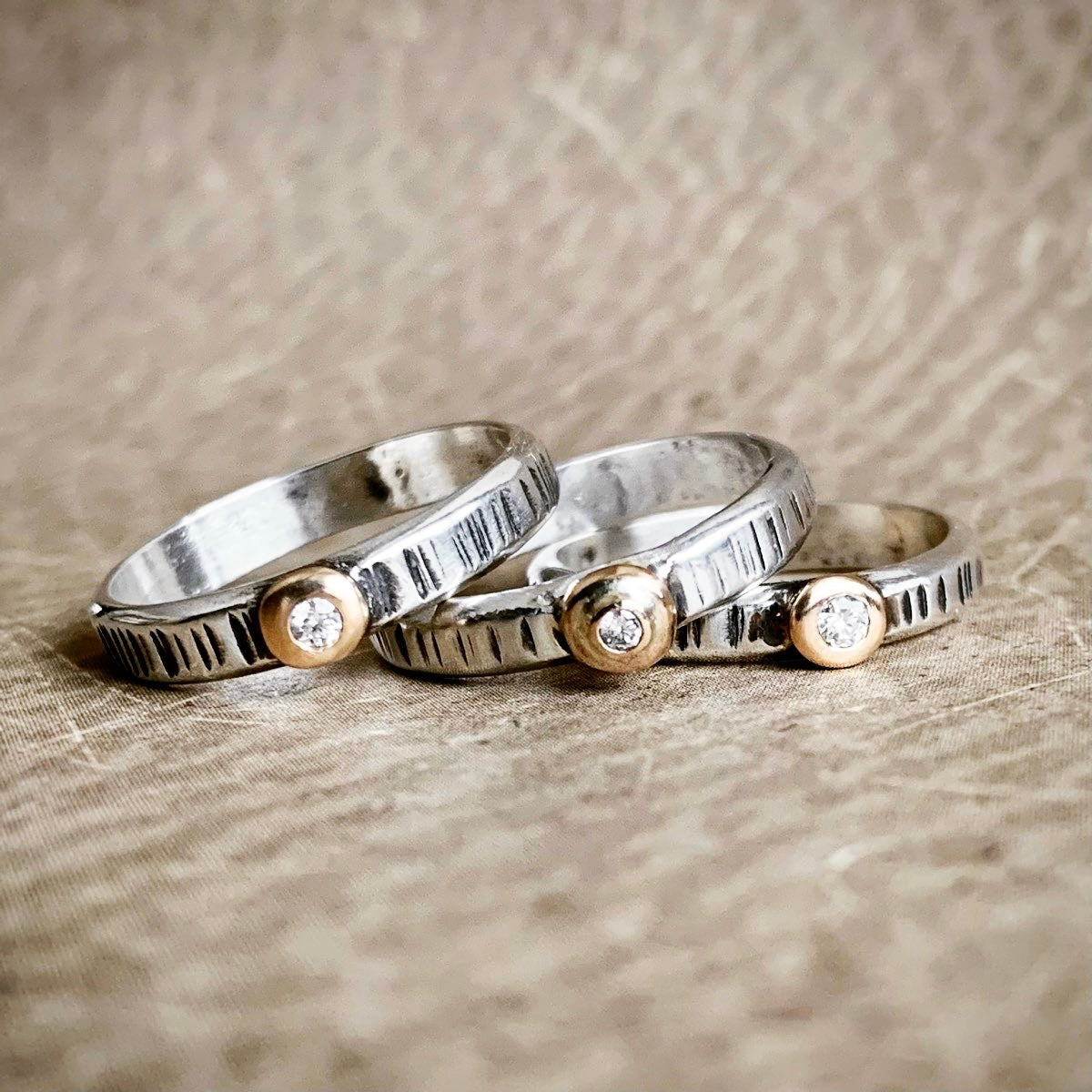 Three silver rings with small diamonds on a textured surface