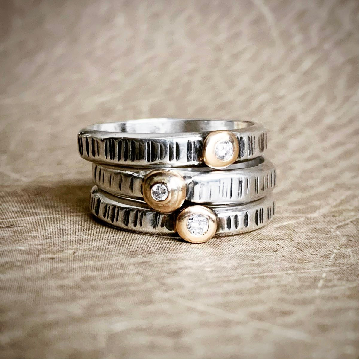 Stack of silver and gold rings with diamond accents on a textured fabric background