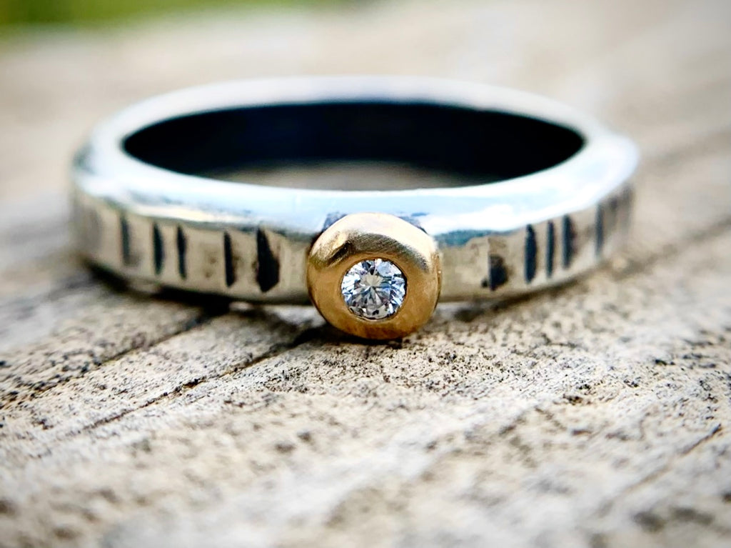 Silver ring with a gold accent and diamond on a wooden surface