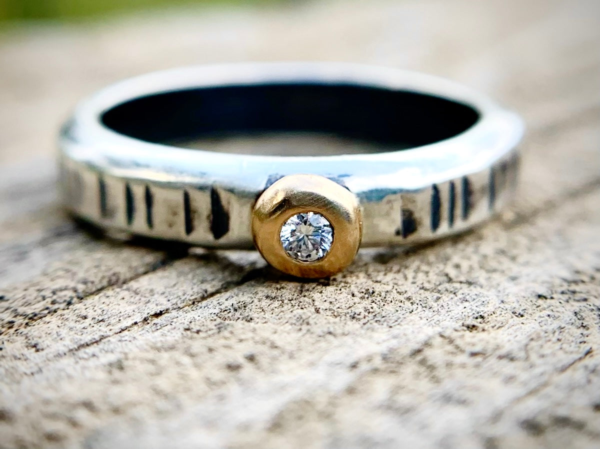 Silver ring with a gold accent and diamond on a wooden surface