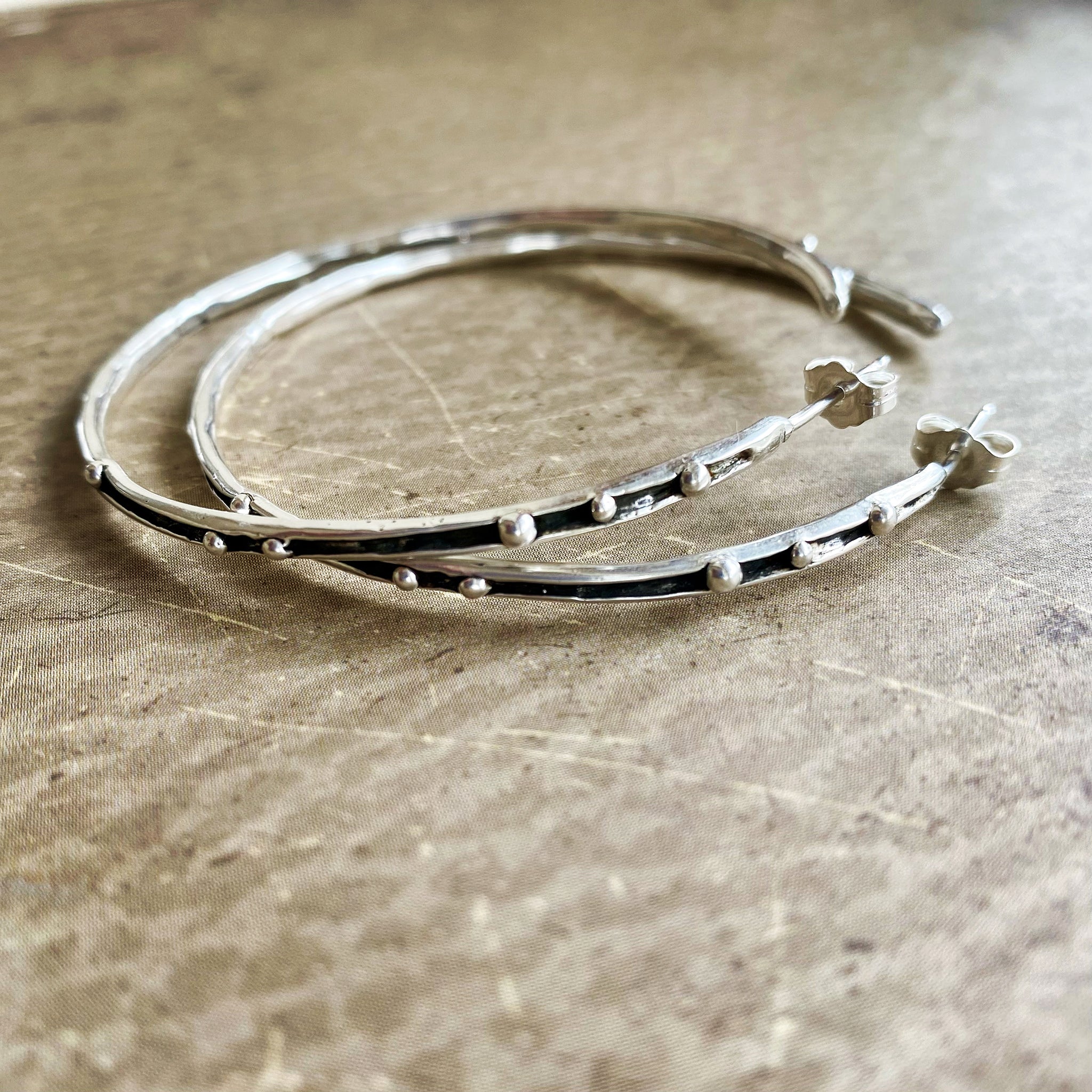 Two silver hoop earrings
 on a textured surface