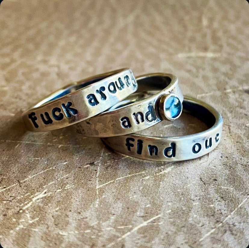 Two silver rings with engraved text on a textured surface