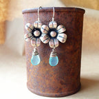 Flower-shaped earrings with blue drops on a rusted metal container.
