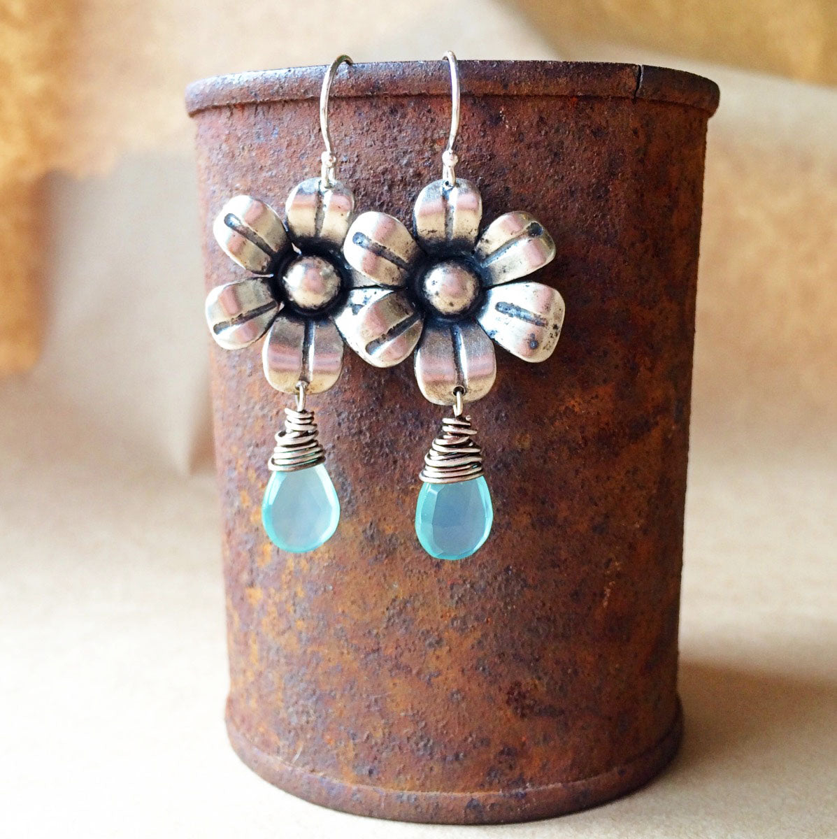 Flower-shaped earrings with blue drops on a rusted metal container.