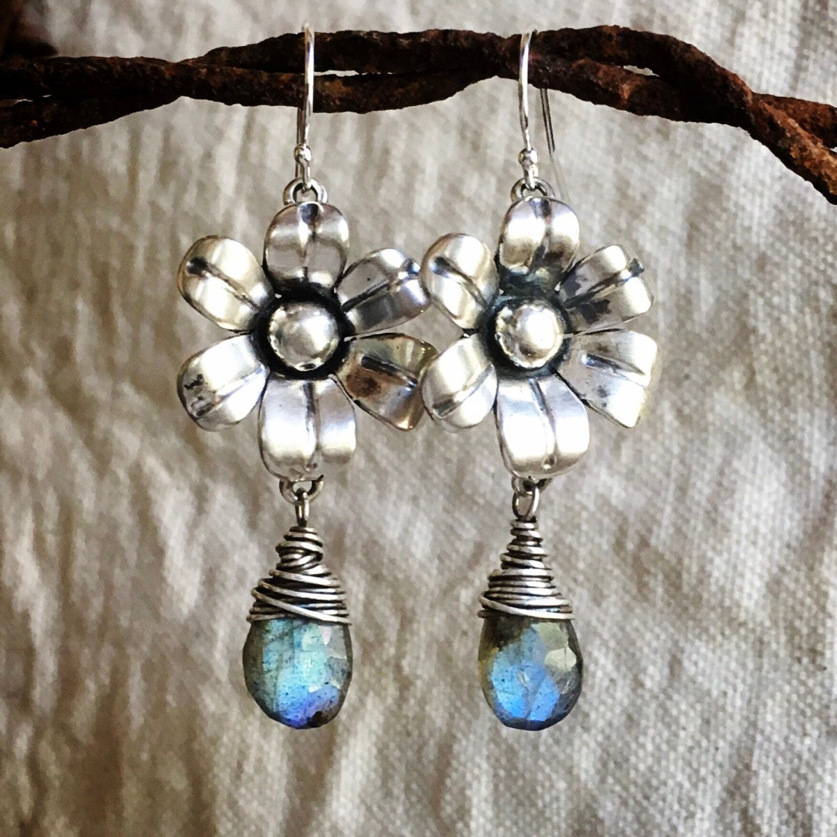 Flower-shaped earrings with Labradorite stones on a textured fabric background