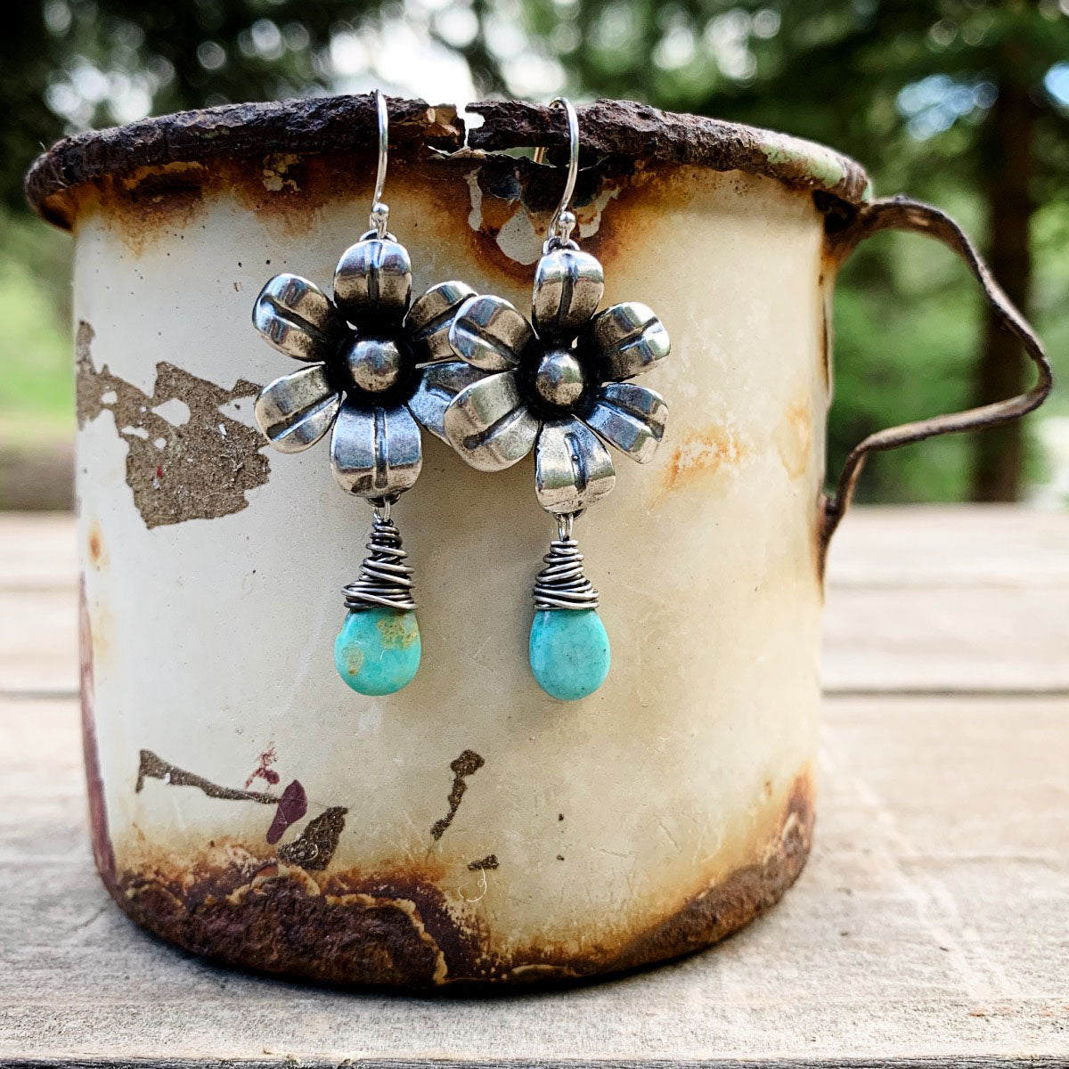 Silver flower earrings with turquoise drops on a rustic mug.