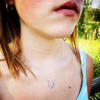 Close-up of a child wearing a silver necklace with a horseshoe pendant outdoors.