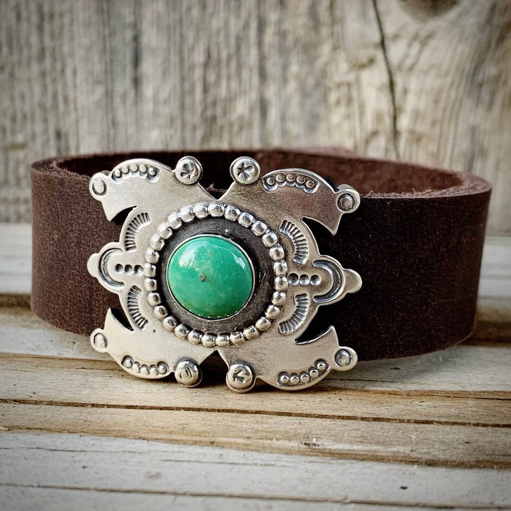 Brown leather belt with a silver and turquoise buckle on a wooden surface