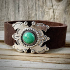 Brown leather belt with a silver and turquoise buckle on a wooden surface