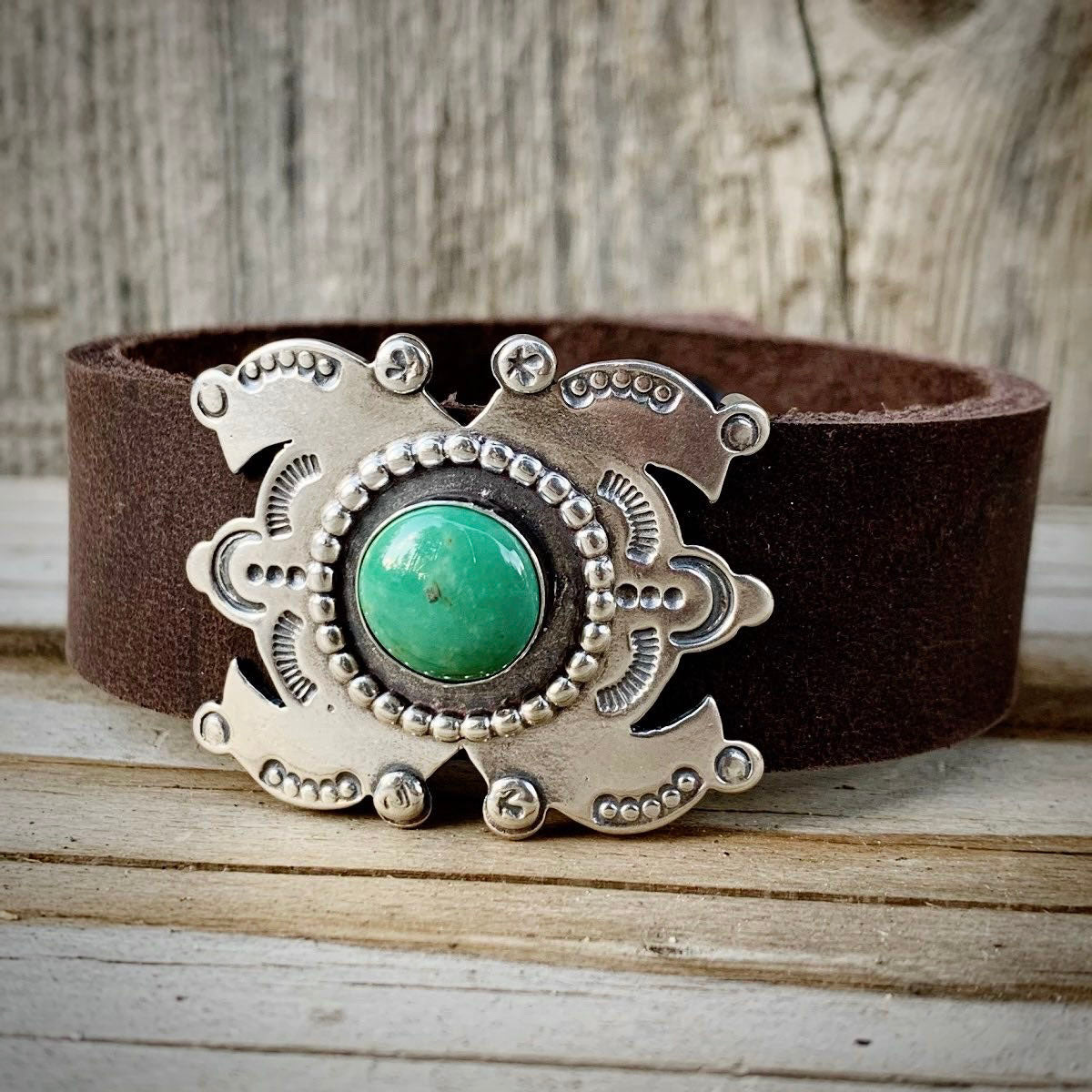 Brown leather belt with a silver and turquoise buckle on a wooden surface