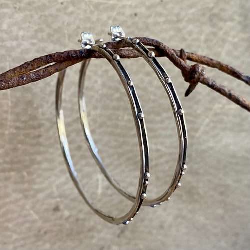 Silver hoop earrings with embedded stones on a rustic background