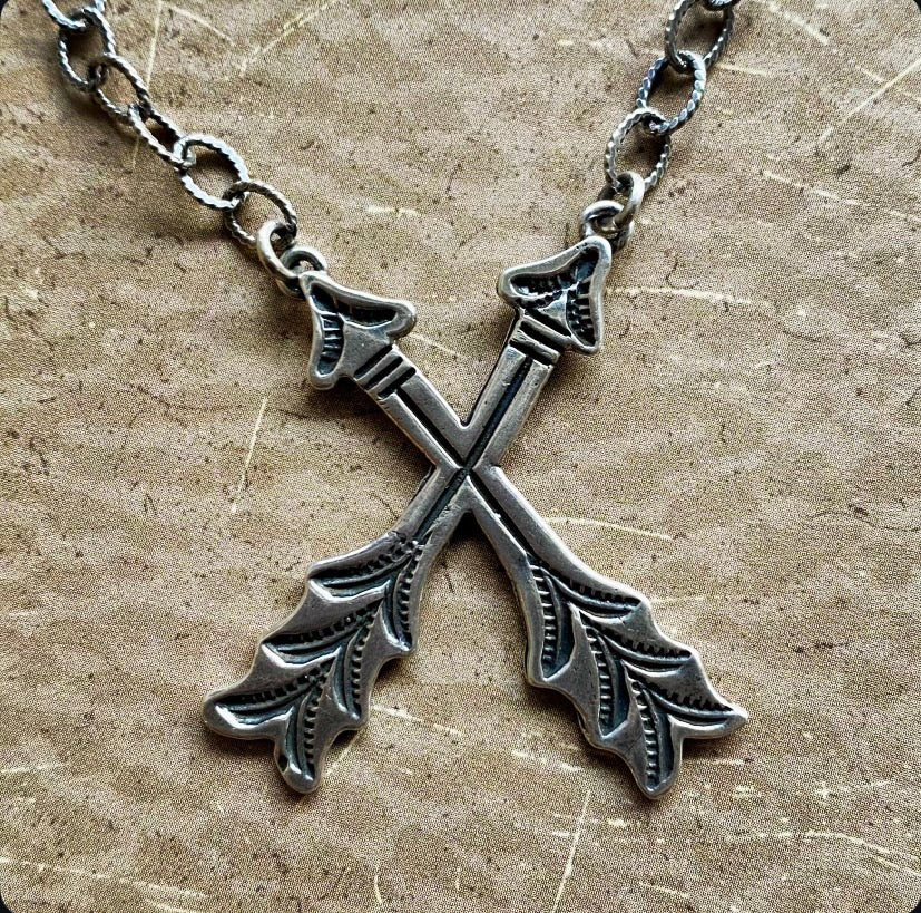 Silver cross arrows-shaped pendant on a chain against a textured beige background