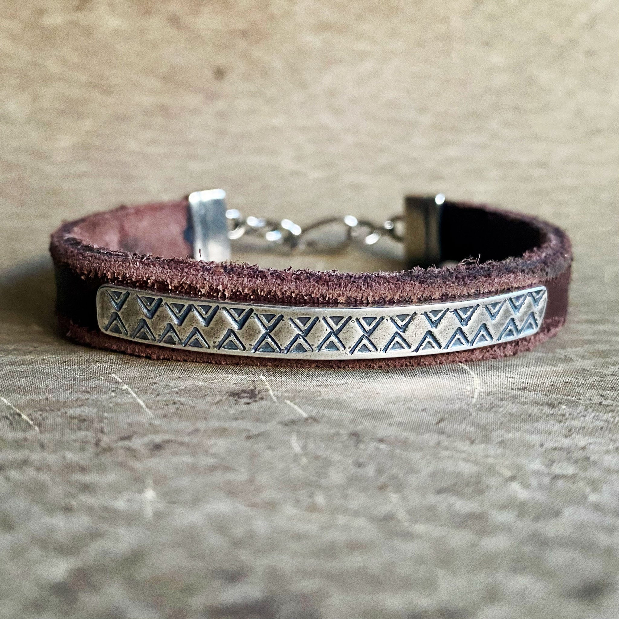 Brown leather bracelet with metal clasp on a textured surface