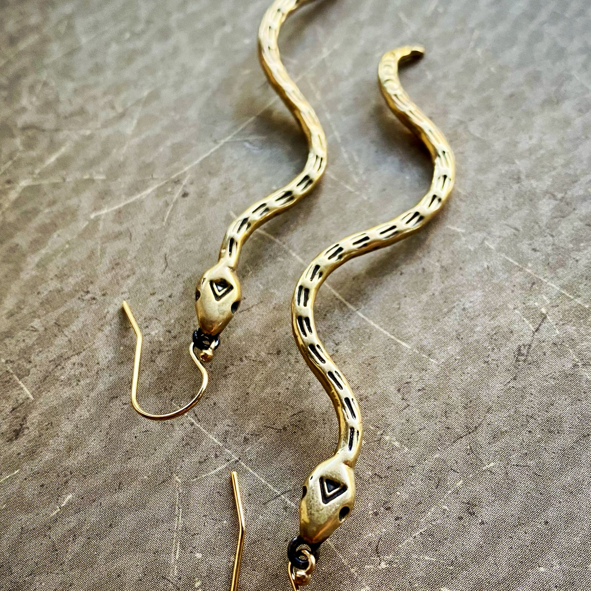 Gold snake-shaped earrings on a textured surface