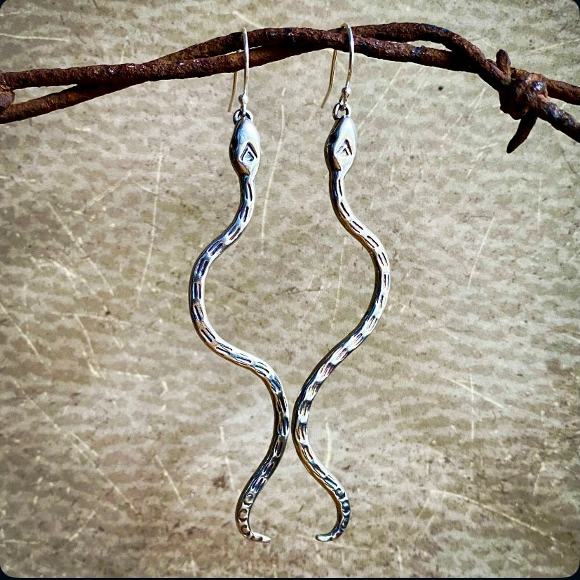 Silver snake-shaped earrings on a textured surface