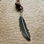Feather-shaped pendant on a leather cord against a textured surface