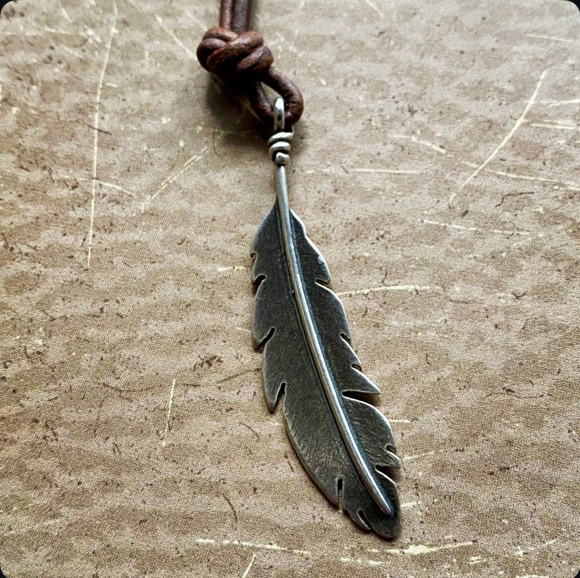 Feather-shaped pendant on a leather cord against a textured surface