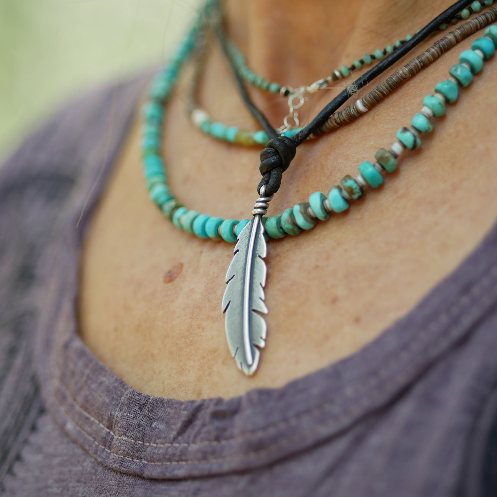 Necklace with a feather pendant and turquoise beads on a person wearing a gray shirt.