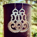 Silver earrings hanging from a dark cylindrical container with a natural background