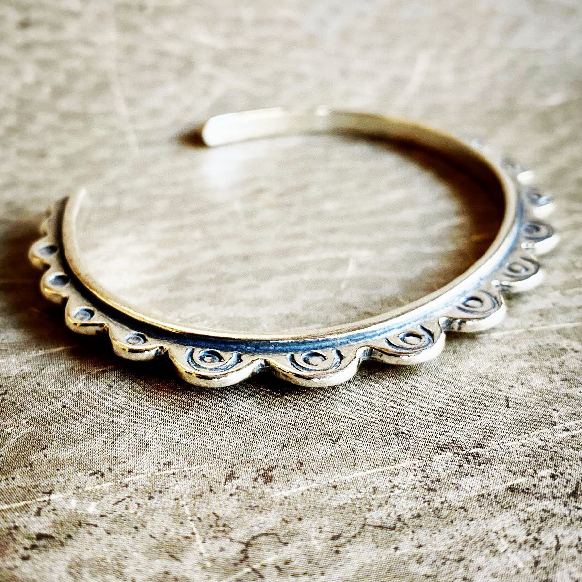 Silver bangle with decorative edge on a textured surface