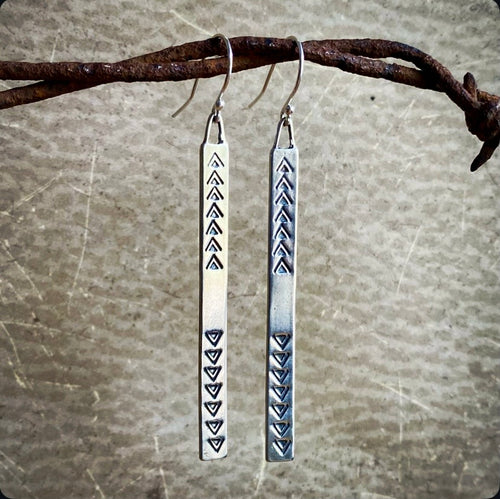 Pair of silver earrings with tribal patterns hanging on a branch.