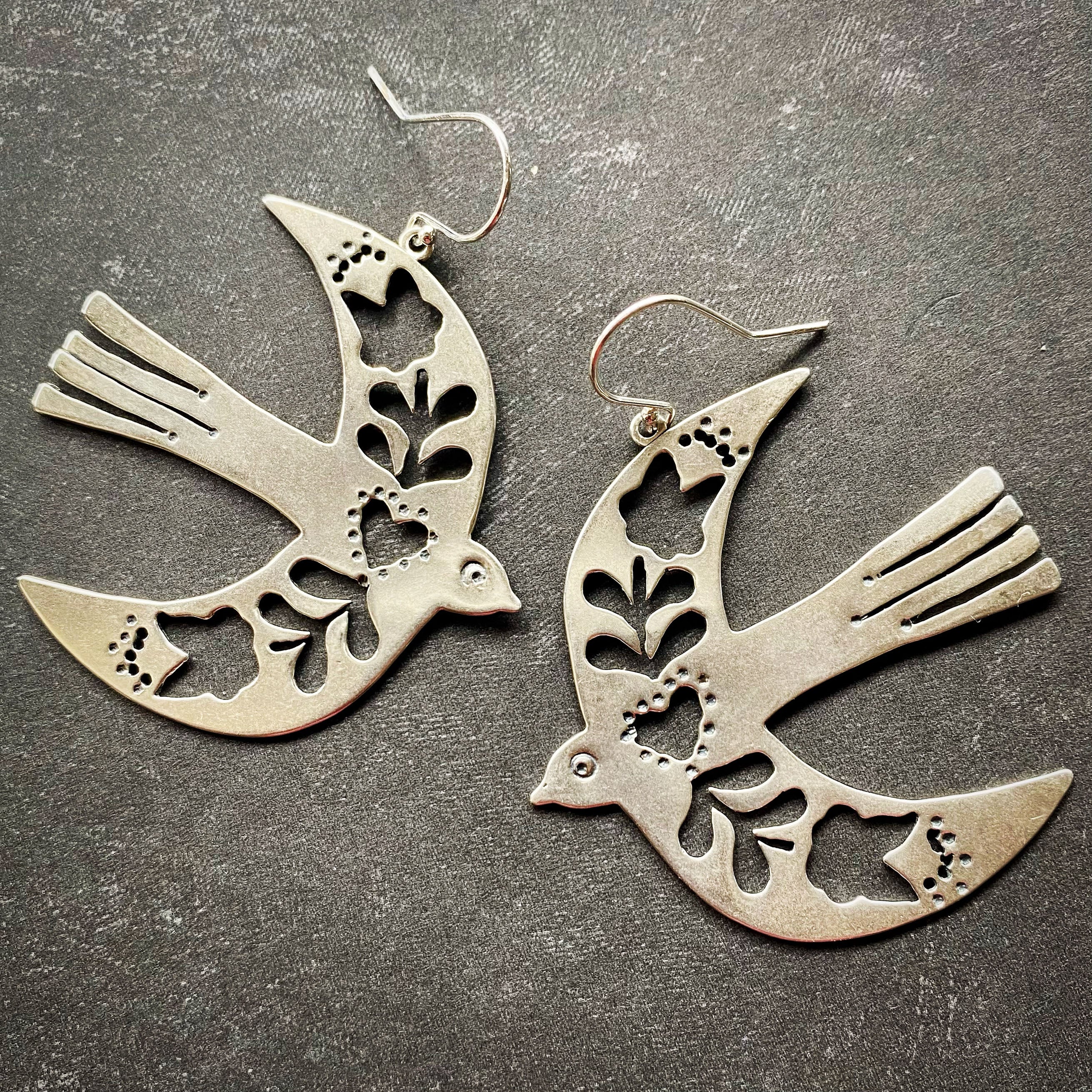 Silver dove-shaped earrings on a dark surface