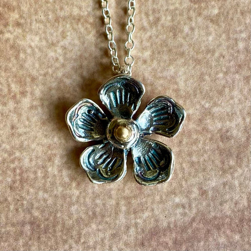 Silver flower-shaped pendant on a chain against a beige background