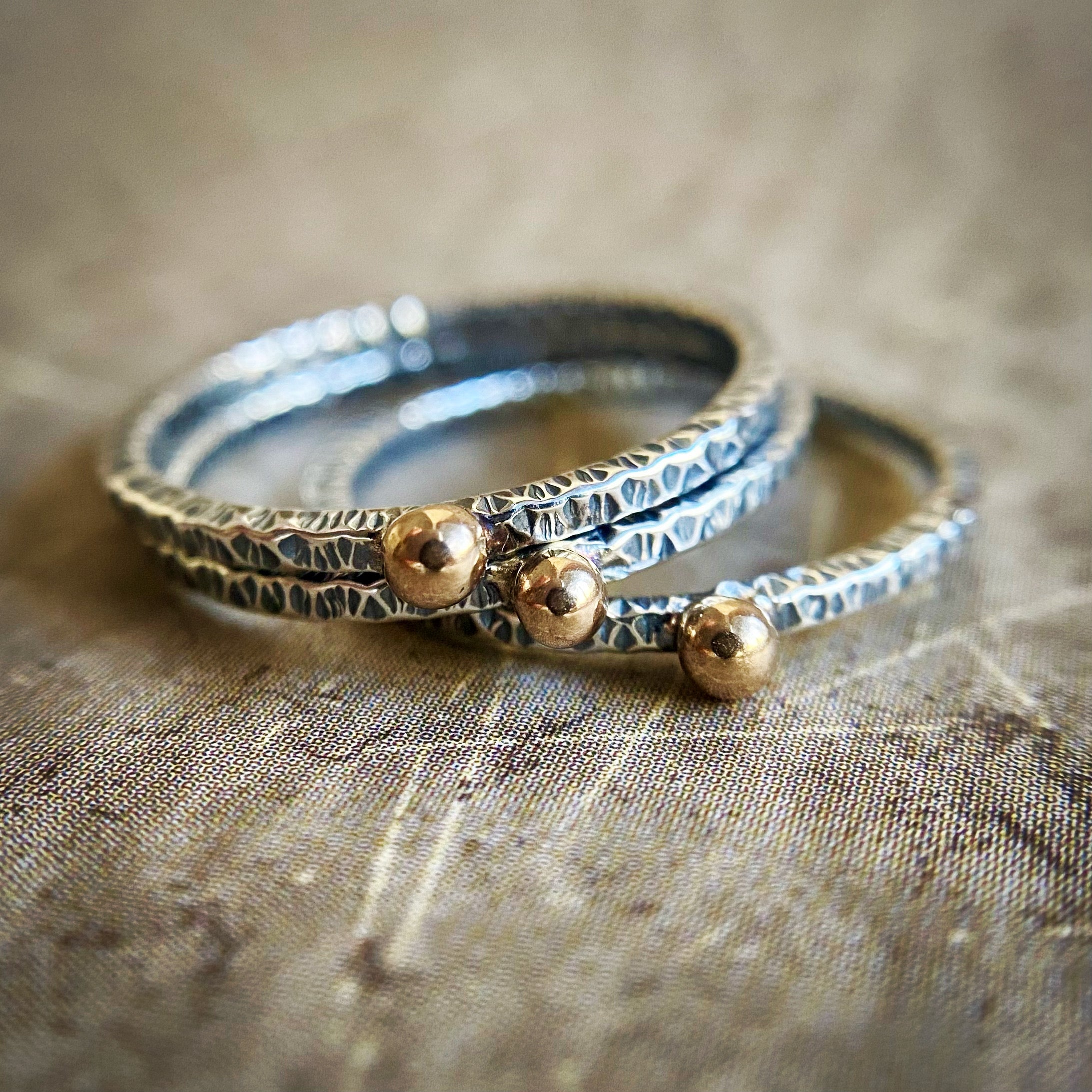 Stack of silver and gold rings on a textured fabric background