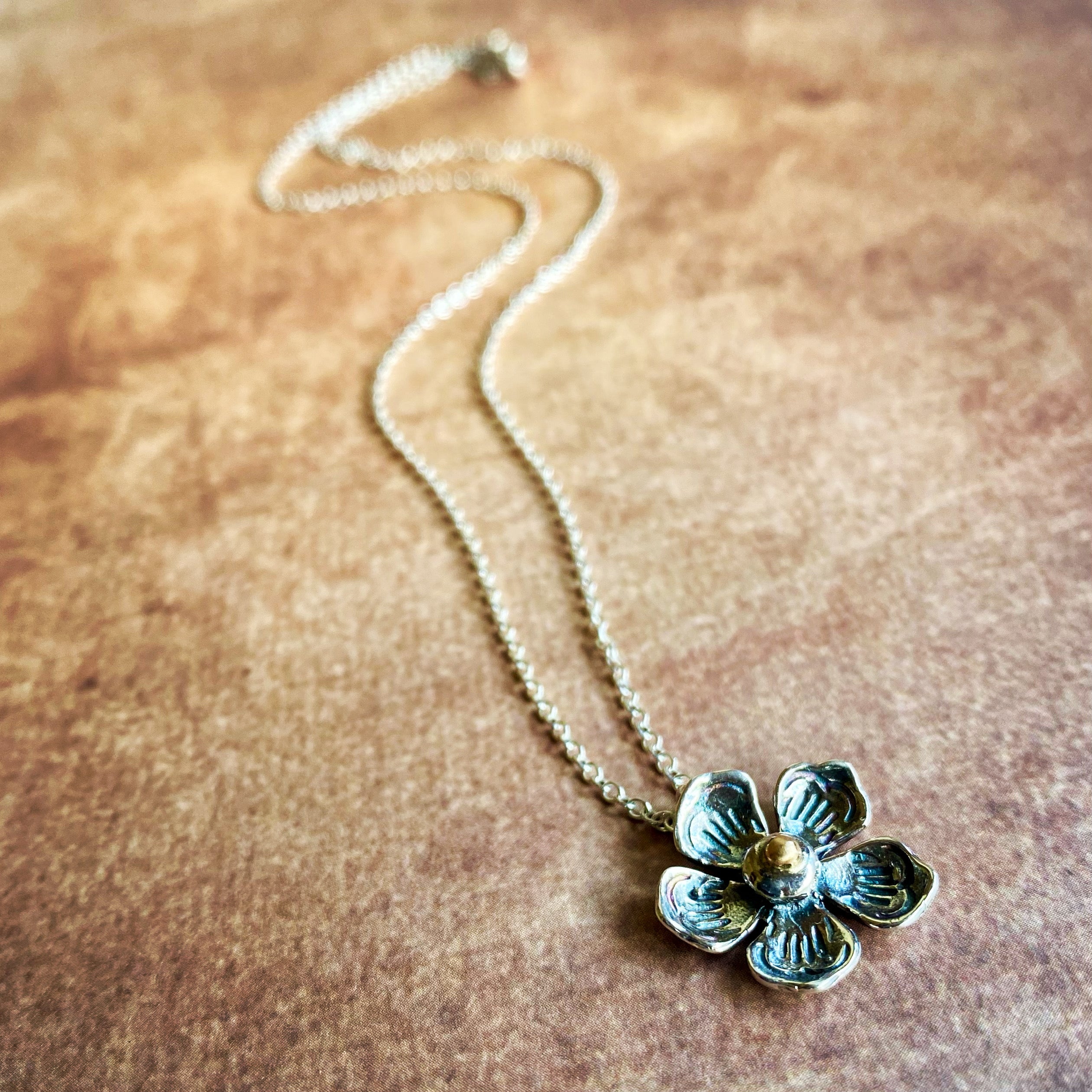 Silver flower pendant necklace on a brown textured surface