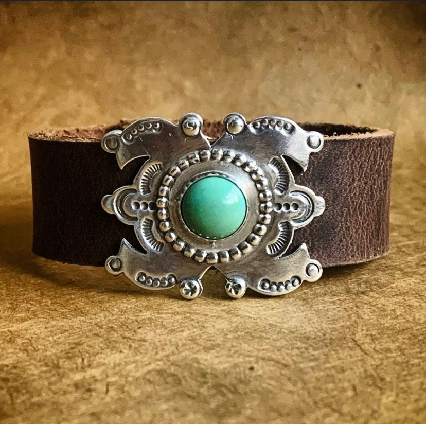 Decorative bracelet with silver design and turquoise stone on a brown background